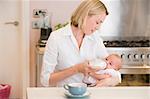 Mother feeding baby in kitchen with coffee