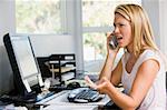 Woman in home office with computer using telephone frowning