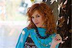 close up of a cute red haired girl with sky-blue scarf necklace near a tree