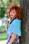 red haired girl in the park standing near the tree with sky-blue scarf