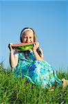 Little girl sitting at meadow and eating watermelon