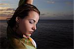 Portrait of young fashion female model relaxing by the ocean at sunset