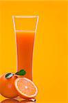 View of long glass filled with fresh juice and some oranges nearby