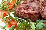 juicy fried beef steak with roocket salad and slced tomatoes