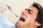 dentist holding a syringe and anesthetizing his terrified patient.