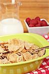 A bowl of cornflakes, milk and raspberries on bamboo mat