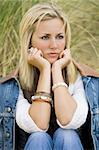 A beautiful blond haired blue eyed model sits thinking amid tall green grass