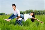 Man giving woman piggyback in meadow, laughing