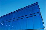 A modern office block with blue glass facade thrusts into the sky