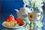 Teapot and strawberry cake, blue background and flowers bouquet.