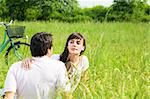 Young couple outdoors sitting in meadow, woman looking around. Copy space