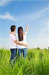 young couple in meadow with hand in air, hugging and smiling. Copy space