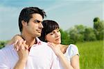 Couple standing in meadow, arm around and looking away. Copy space