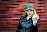 Aggressive young woman showing middle finger (brickwall as background)