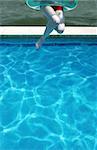 Young woman jumps into a swimming pool on a hot summer day - perfect for generic holiday and travel usage such as spring break