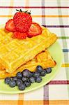 Waffles, blueberries and strawberries on green plate on square mat background. Shallow depth of field