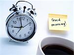 An alarm clock, a cup of fresh coffee and a yellow note with this text: 'Good morning!'