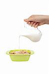Pouring milk in a cereals bowl isolated on white background. Shallow depth of field