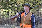 Middle-aged man hunting in a field wearing an orange safety vest