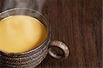 A macro, selective focus image of coffee with milk, in a wooden mug on a wood table.  Lots of copyspace available - Shallow depth of field with the focus on the handle.