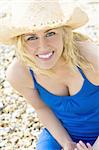 A beautiful blond haired blue eyed model wearing a straw cowboy hat and with a gorgeous smile shot in close up at the beach and illuminated with natural light