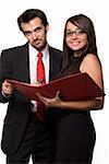 Two business people wearing black business attire attractive brunette woman with eyeglasses and one man with red tie both smiling looking at a red binder