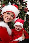 Beautiful mommy and precious daughter Santas in front of Christmas tree