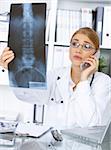 Portrait of female doctor examining x-ray picture and talking cell