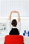 Rear view of young businesswoman sitting at desk stretching. Copy space