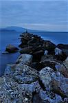 Picture of a rocky formation extending into the sea. The late evening colours create a sense of serenity and peace. Room for text on top