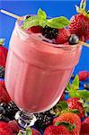 A glass of berry smoothie surrounded by fresh fruits