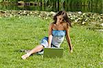 cute brunette in casual dress standing alone on the grass and working on the computer