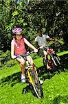 Teenage girl and her father riding bicycles in summer park