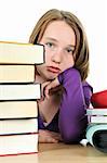 Frustrated teenage girl studying at the desk with big stack of books