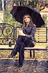 Girl with umbrella sitting on bench at autumn park. it's raining