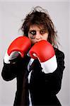 businesswoman wearing boxing gloves with bruised eye. grey background.