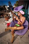 Black woman kissing rifle in front of house with messy yard