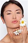 Studio shot of a beautiful young Japanese woman holding daisies and blowing a kiss to the camera.
