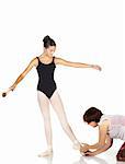 Young caucasian ballerina girl on white background and reflective white floor showing various ballet steps and positions being corrected by teacher. Not Isolated.