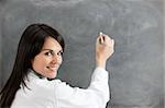rear view of female teacher in lab clothes holding chalk against blank blackboard. Copy space