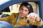 young man sitting inside car showing keys to new car