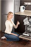 The young joyful woman sits near to the dishwasher on kitchen