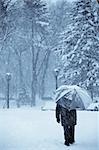 lonely old man with umbrella walking under the snow