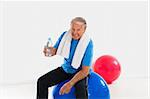 senior man sitting on fitness ball in gym and holding water bottle. Copy space