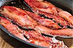 Bacon strips sizzling on a frying pan