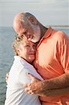 Senior couple in a loving embrace with the ocean in the background.