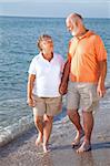 Vacationing senior couple takes a romantic stroll on the beach.
