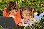 Woman and little girl relaxing on the spring flower field using a laptop