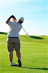 Young male golfer hitting the ball from the fairway on a beautiful summer day