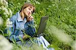 The beautiful girl with the laptop in park sits in a green grass